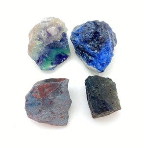 May include: Four rough, natural, tumbled stones in various colours. A green, purple, and white fluorite, a blue sodalite, a dark grey hematite, and a black obsidian.