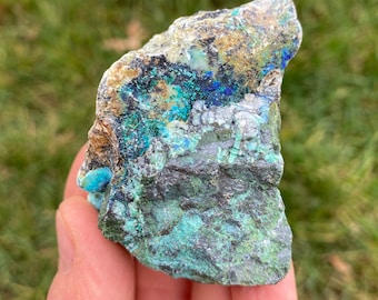 May include: A rough, irregular shaped rock with a mix of green, blue, and brown colors. The rock has a rough, textured surface and appears to be a mineral specimen.