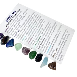 May include: A set of 10 tumbled crystals for ADHD and concentration. The crystals are amethyst, hematite, lapis lazuli, fluorite, lepidolite, green aventurine, black tourmaline, aquamarine, and smoky quartz. The crystals are arranged in a row on a white background. The text on the card reads: "ADHD Set Attention & Concentration".