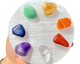 May include: A white selenite charging plate with seven chakra crystals: amethyst, sodalite, green aventurine, citrine, carnelian, red jasper, and clear quartz.