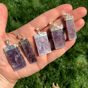 May include: Six silver pendants with purple lepidolite stones. The pendants are rectangular and have a smooth, polished finish. The stones are a light purple color with a slight shimmer.