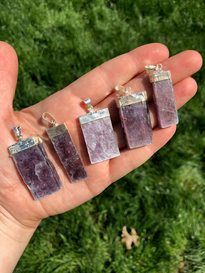 May include: Six silver pendants with purple lepidolite stones. The pendants are rectangular and have a smooth, polished finish. The stones are a light purple color with a slight shimmer.