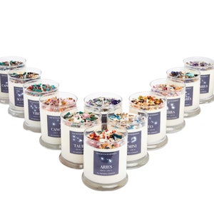 May include: Twelve glass candle jars arranged in a V-shape. Each jar contains a white candle with embedded crystals and dried flowers. The jars are labeled with the twelve zodiac signs: Aries, Taurus, Gemini, Cancer, Leo, Virgo, Libra, Scorpio, Sagittarius, Capricorn, Aquarius, and Pisces.