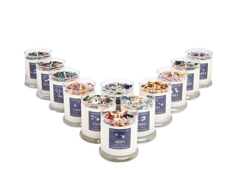 May include: Twelve glass candle jars arranged in a V-shape. Each jar contains a white candle with embedded crystals and dried flowers. The jars are labeled with the twelve zodiac signs: Aries, Taurus, Gemini, Cancer, Leo, Virgo, Libra, Scorpio, Sagittarius, Capricorn, Aquarius, and Pisces.