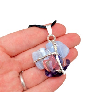 May include: A silver wire wrapped pendant with blue, pink, and purple gemstones. The pendant is on a black cord.