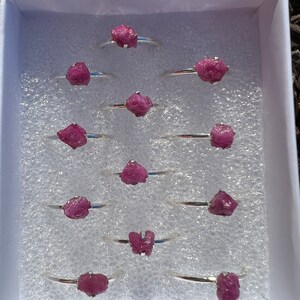 May include: A set of ten silver rings with pink ruby stones. The rings are displayed in a white box with a white foam lining.