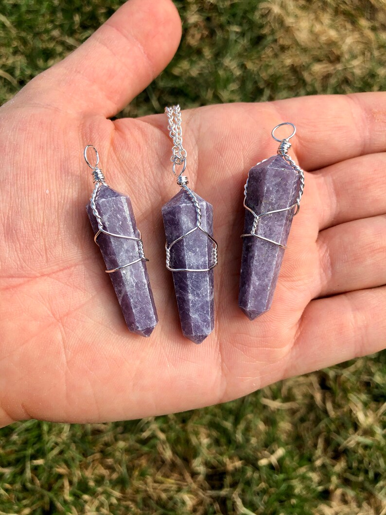 May include: Three purple lepidolite crystal pendants wrapped in silver wire. The pendants are of different sizes and are hanging from a silver chain.