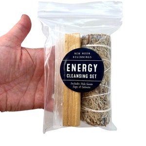 Pu&ograve; includere: Un sacchetto di plastica trasparente contenente un set di strumenti per la pulizia energetica. Il set include un bastoncino di selenite bianco, un bastoncino di palo santo marrone e un mazzo di salvia bianca. Il sacchetto ha un'etichetta che recita "New Moon Beginnings Energy Cleansing Set Includes: Palo Santo Sage & Selenite"