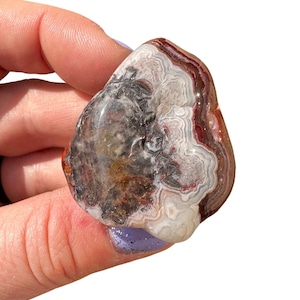 May include: A smooth, polished agate stone with a swirling pattern of white, brown, and red. The stone has a natural, organic shape.