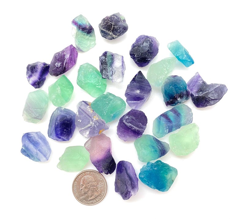 Puede incluir: Una colecci&oacute;n de cristales de fluorita en varios tonos de verde, azul y morado. Los cristales son &aacute;speros y tienen un aspecto natural sin pulir.
