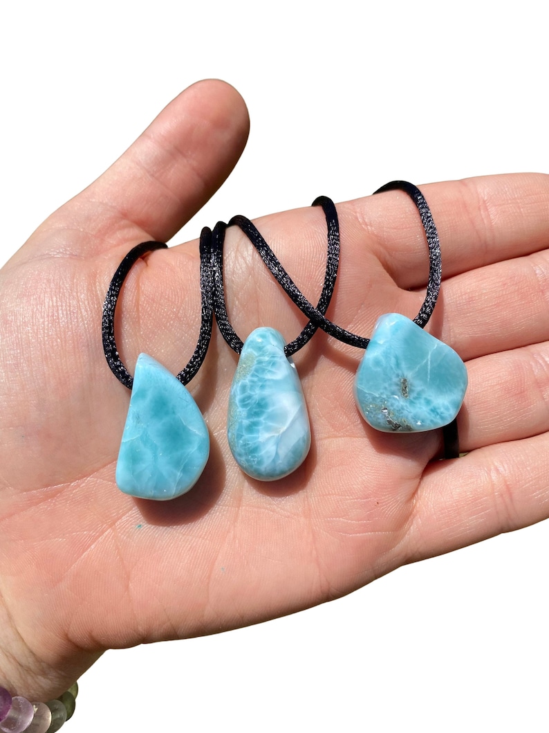 May include: Three blue and white gemstone pendants on black cords. The pendants are teardrop shaped and have a marbled appearance.