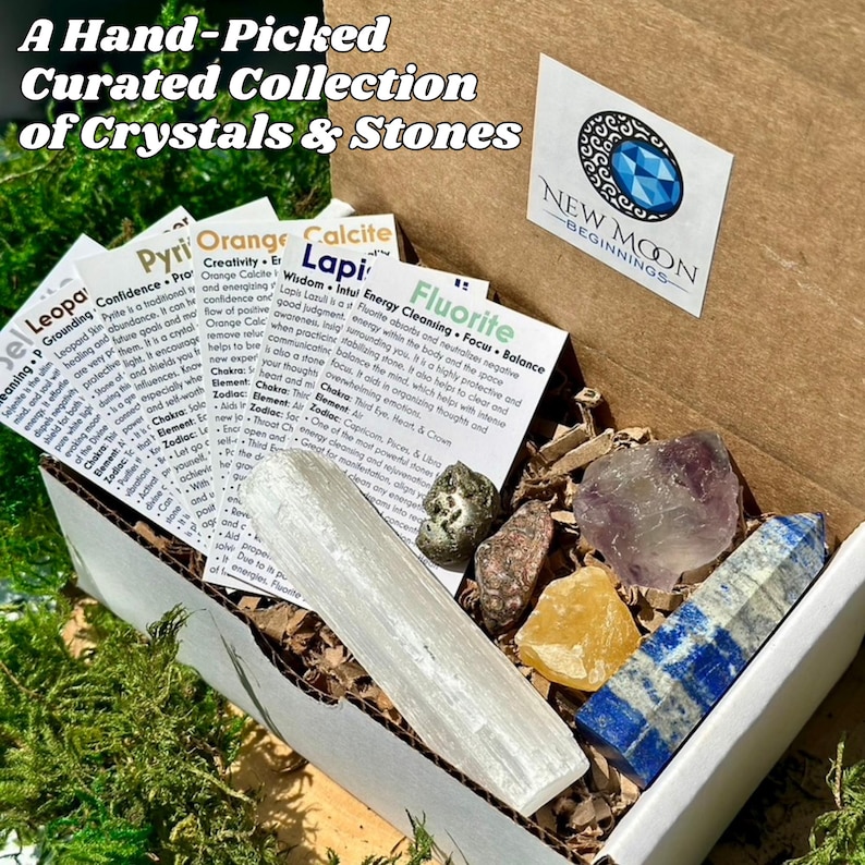 May include: A curated collection of crystals and stones in a white box. The box contains various crystals, including a clear selenite wand, a purple amethyst, a yellow calcite, and a blue lapis lazuli. The box also includes informational cards.