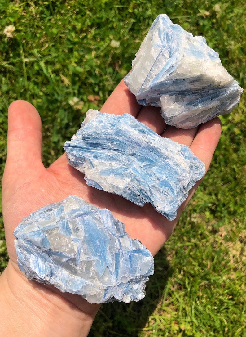 May include: Three blue kyanite crystal specimens with a white, layered, and striated texture. The crystals are rough and natural, with a light blue color.