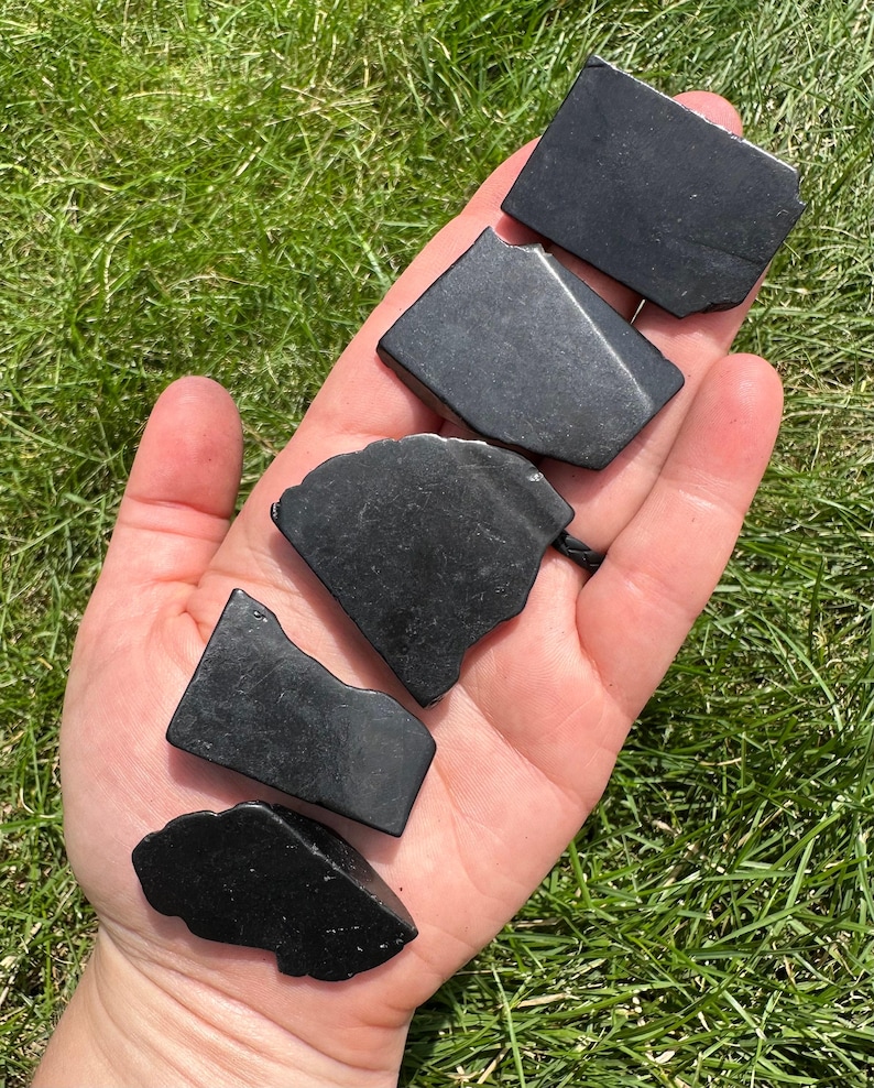 May include: Five black obsidian stones of various shapes and sizes. The stones are smooth and polished, with a deep black color.