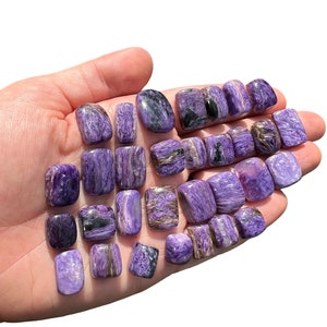 May include: A collection of tumbled, polished, purple and black spectrolite stones. The stones are smooth and have a shimmering, iridescent effect.