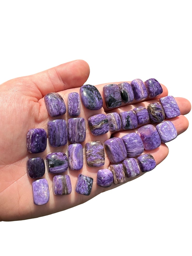 May include: A collection of tumbled, polished, purple and black spectrolite stones. The stones are smooth and have a shimmering, iridescent effect.