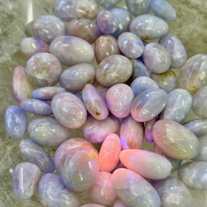 May include: A collection of polished, oval-shaped gemstones in shades of pale blue, pink, and white. The stones have a smooth, glossy texture and vary in size. The overall effect is a soft, pastel color palette.