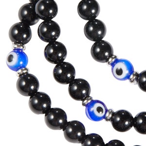May include: Close-up of three strands of black beaded bracelets. Each strand features large, glossy black beads. Interspersed are blue and white evil eye beads, adding a pop of color. The bracelets are strung on a silver-toned metal.
