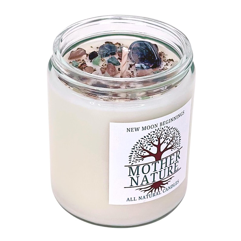 May include: A white candle in a clear glass jar with a label that reads "New Moon Beginnings" and "Mother Nature All Natural Candles". The candle has a tree design with roots and a green and brown color scheme. The jar contains small crystals and a wick.