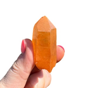May include: A large, orange crystal point with a pointed tip and a smooth, polished surface.