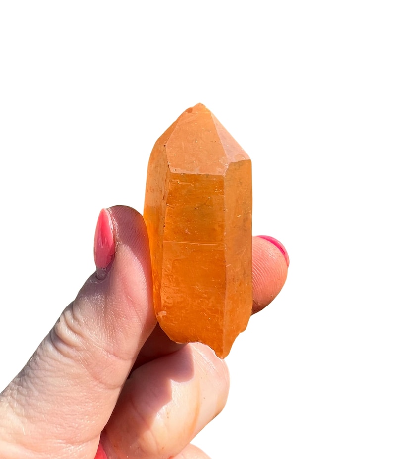 May include: A large, orange crystal point with a pointed tip and a smooth, polished surface.
