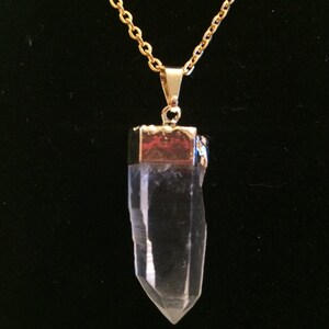 Puede incluir: Un collar de cadena dorada con un colgante de cristal de cuarzo transparente. El colgante est&aacute; facetado y tiene una tapa dorada en la parte superior.