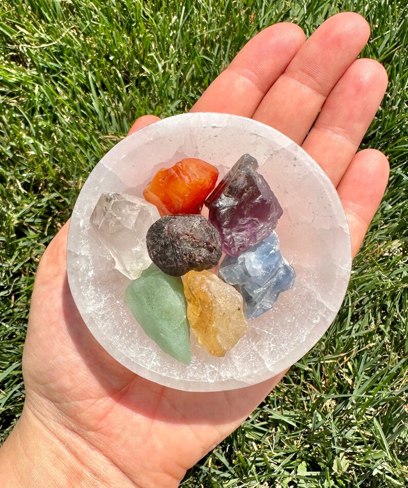 May include: A white selenite bowl filled with seven small, colourful crystals. The crystals are red, orange, yellow, green, blue, purple, and clear.