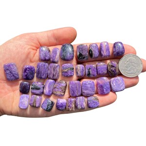 May include: A collection of 18 purple and black tumbled stones. The stones are smooth and polished, and they have a variety of patterns and textures. The stones are about the size of a quarter.
