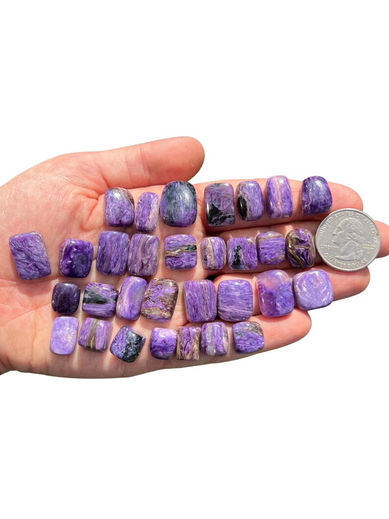 May include: A collection of 18 purple and black tumbled stones. The stones are smooth and polished, and they have a variety of patterns and textures. The stones are about the size of a quarter.