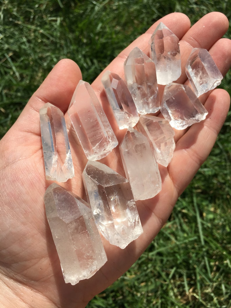 May include: A collection of clear quartz crystal points, also known as rock crystals, in various sizes and shapes. The crystals are arranged in a hand, showcasing their natural beauty and clarity.