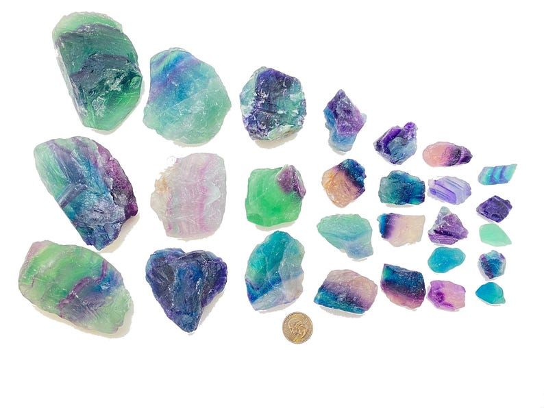 Puede incluir: Una colecci&oacute;n de 25 cristales de fluorita en varios tonos de verde, azul y morado. Los cristales son &aacute;speros y tienen un aspecto natural sin pulir.