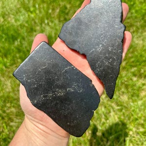 May include: Two pieces of black obsidian, one shaped like a triangle and the other a rectangle, are held in a hand.