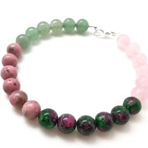 May include: A green, pink, and green gemstone bracelet with a silver clasp. The bracelet is made of round beads.