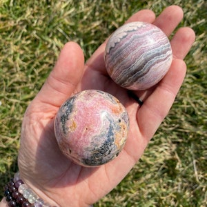 May include: Two pink and black striped spheres of polished gemstone. The spheres are about the size of a golf ball and are held in a person's hand.