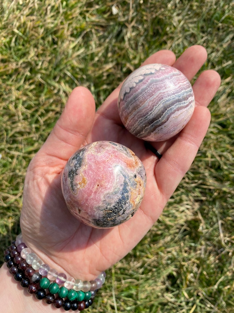 May include: Two pink and black striped spheres of polished gemstone. The spheres are about the size of a golf ball and are held in a person's hand.