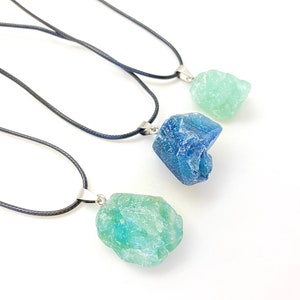 Puede incluir: Tres collares con colgantes de cristal de diferentes colores. Los collares son cordones negros con cierres plateados. Los colgantes son azul claro, azul oscuro y verde claro.