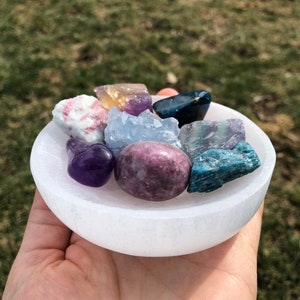 Pu&ograve; includere: Un piatto di ricarica in selenite bianco con una variet&agrave; di cristalli, tra cui ametista, fluorite, celestite e cianite.
