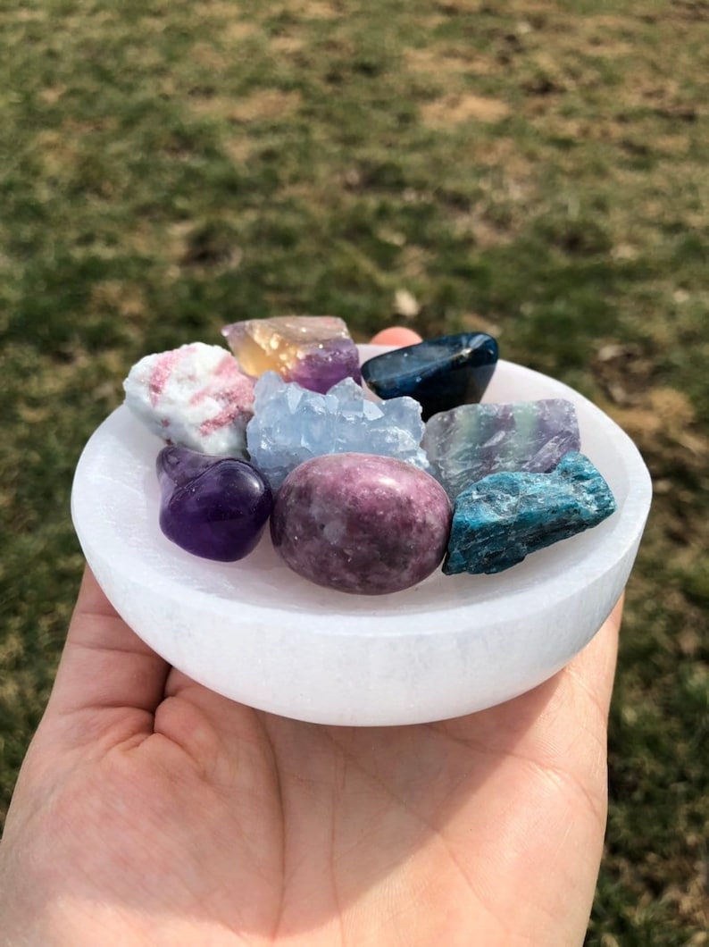 Pu&ograve; includere: Un piatto di ricarica in selenite bianco con una variet&agrave; di cristalli, tra cui ametista, fluorite, celestite e cianite.