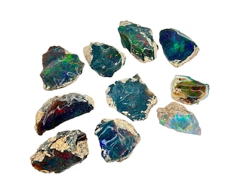 May include: A collection of ten rough, natural black opal stones with iridescent green, blue, and red hues. The stones are various sizes and shapes, and some have a rough, textured surface.