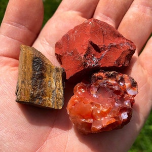 May include: Three rough-cut gemstone crystals: a red jasper, a carnelian, and a tiger's eye.