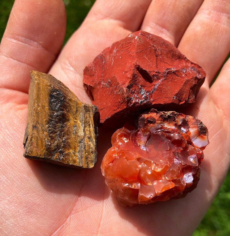 May include: Three rough-cut gemstone crystals: a red jasper, a carnelian, and a tiger's eye.