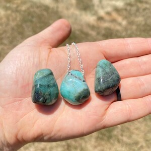 Puede incluir: Tres piedras de esmeralda verde en un collar de cadena de plata. Las piedras est&aacute;n pulidas y tienen un acabado liso y pulido.