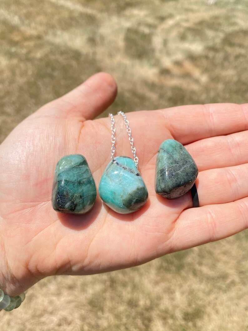 Puede incluir: Tres piedras de esmeralda verde en un collar de cadena de plata. Las piedras est&aacute;n pulidas y tienen un acabado liso y pulido.