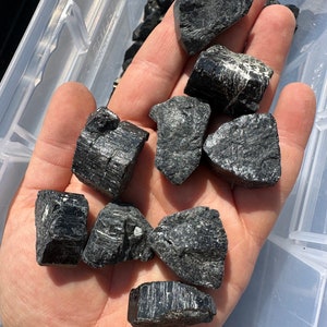May include: A collection of black tourmaline crystals, also known as schorl, in various shapes and sizes. The crystals have a dark, opaque appearance and a rough, natural texture.