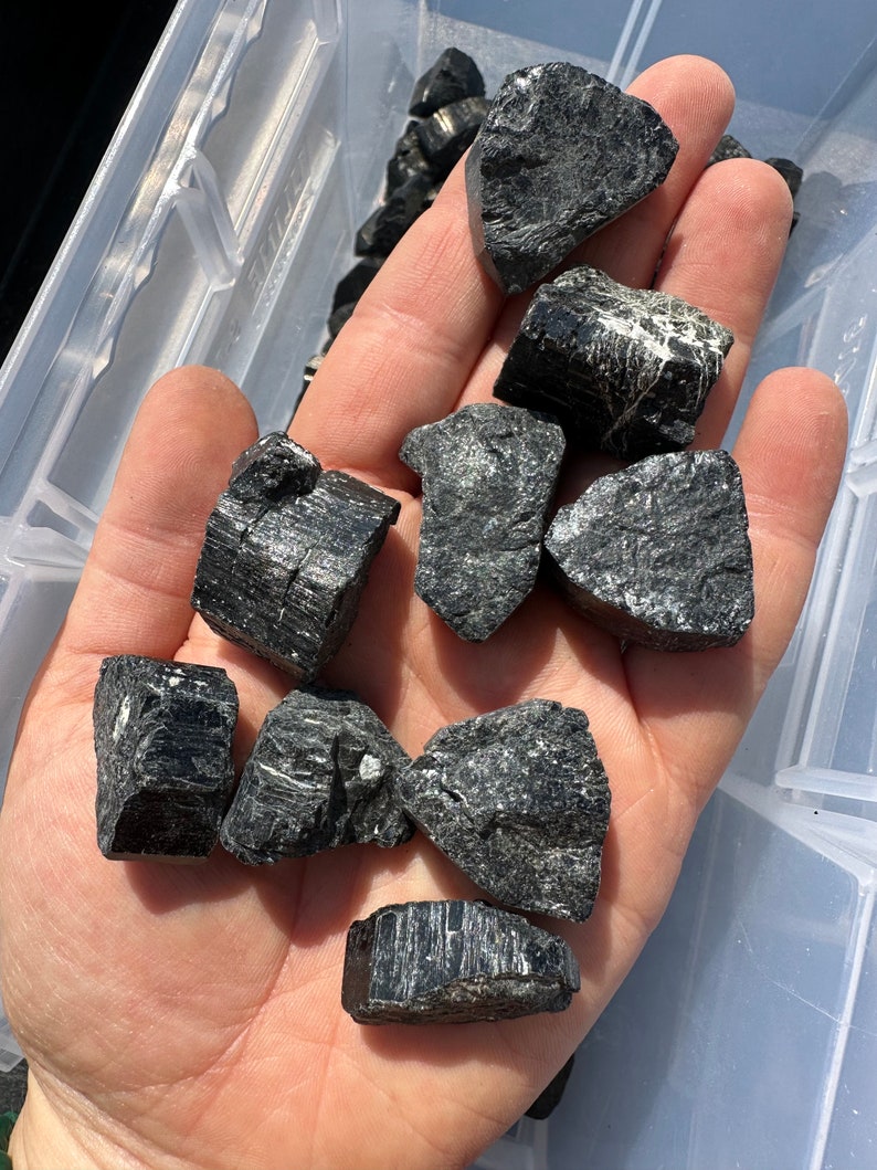 May include: A collection of black tourmaline crystals, also known as schorl, in various shapes and sizes. The crystals have a dark, opaque appearance and a rough, natural texture.