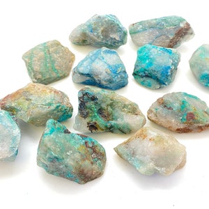 May include: A collection of ten rough, natural, turquoise and white chrysocolla stones. The stones are various sizes and shapes, with a mix of blue, green, and white colors.