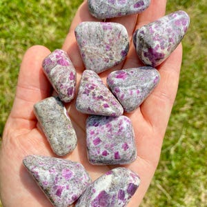 May include: A collection of tumbled ruby in kyanite stones. The stones are a mix of white and gray with pink and red ruby inclusions.