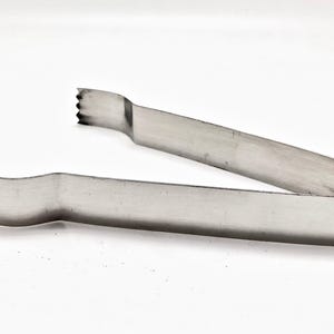 May include: Silver metal ice tongs with a serrated edge on each end. The tongs are designed to grip and lift ice cubes.