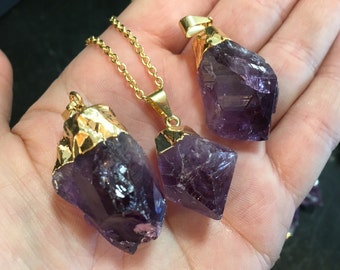 Könnte beinhalten: Drei Amethyst-Kristall-Anhänger mit vergoldeten Einstellungen. Die Kristalle sind in verschiedenen Größen und Formen und alle an goldenen Ketten befestigt.