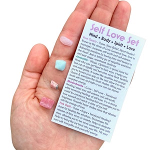 May include: A set of four crystals for self-love, including rose quartz, amazonite, rhodochrosite, and pink opal. The crystals are arranged on a white card with text describing the properties of each crystal.